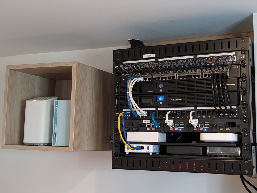 Rack mural avec le nouveau tiroir 1U GeeekPi installé : trois Raspberry Pi 5 montés côte à côte et étiquetés (COQUILLE, WORKER1, WORKER2), sous les panneaux de raccordement et les deux onduleurs CyberPower, avec le cube mural IKEA (NAS et nœud Helix Fi) juste à côté